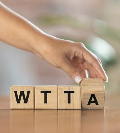 Hand legt houten blokjes met de letters WTTA op tafel